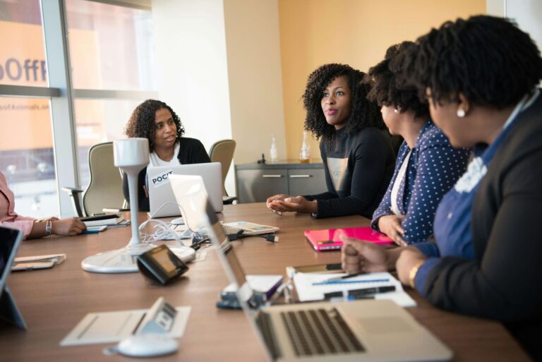 A group of women engaged in discussion around a conference table, collaborating on a project.