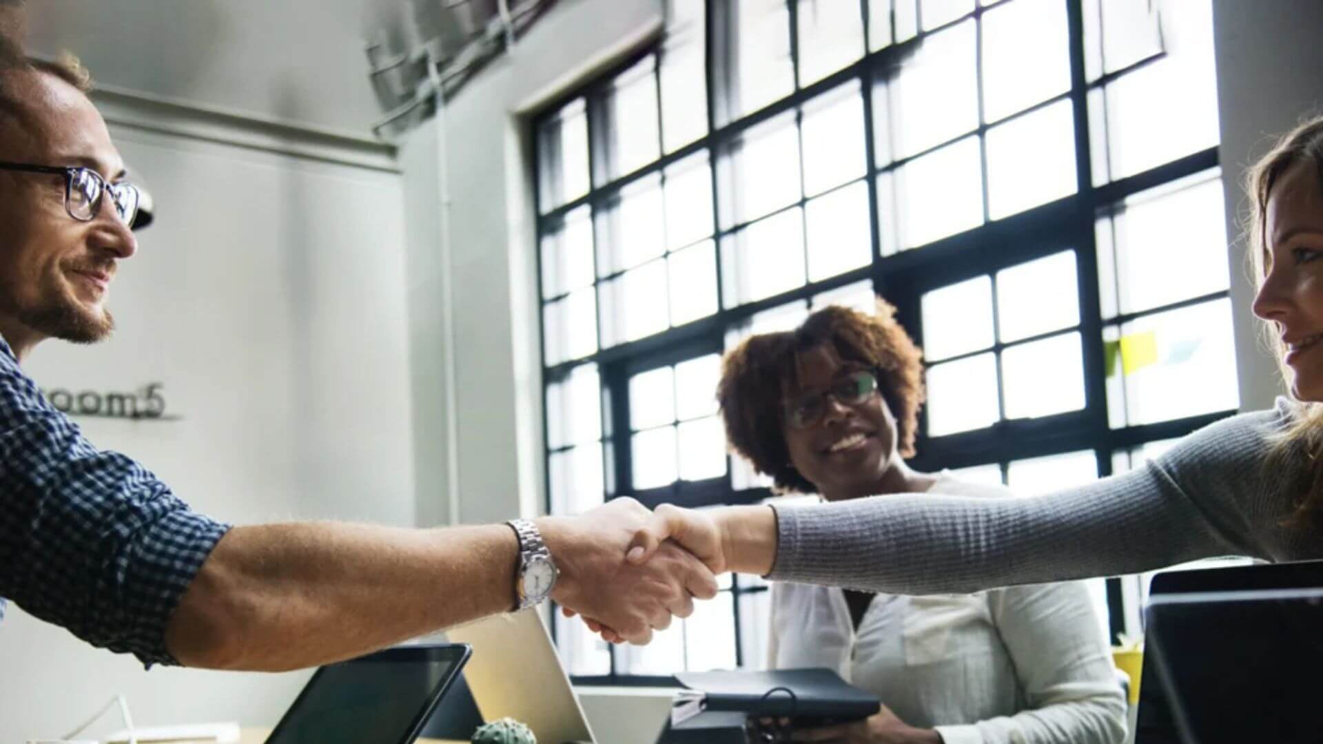 A man and woman engaged in a handshake inside an office, representing collaboration and mutual agreement.