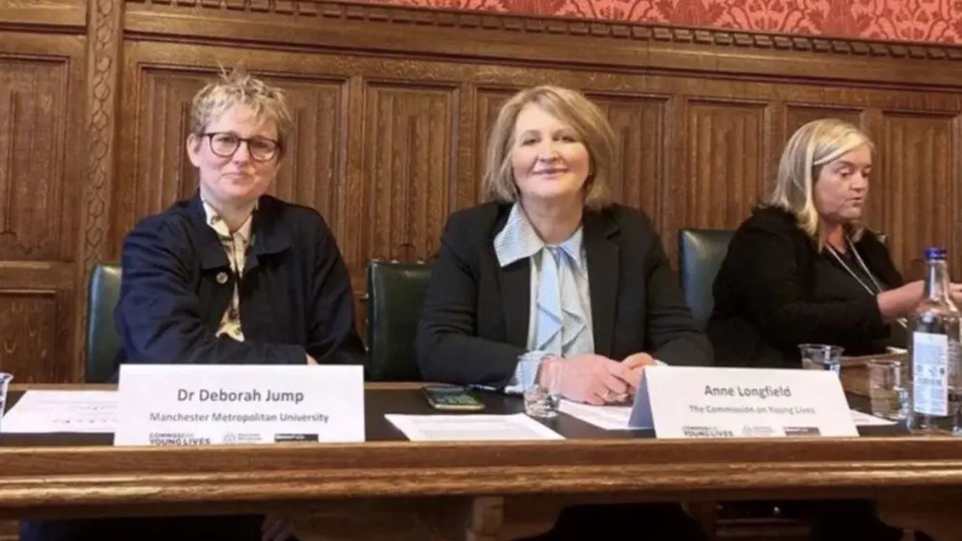 Three women sitting together at a table, with a microphone set up for their discussion or presentation.