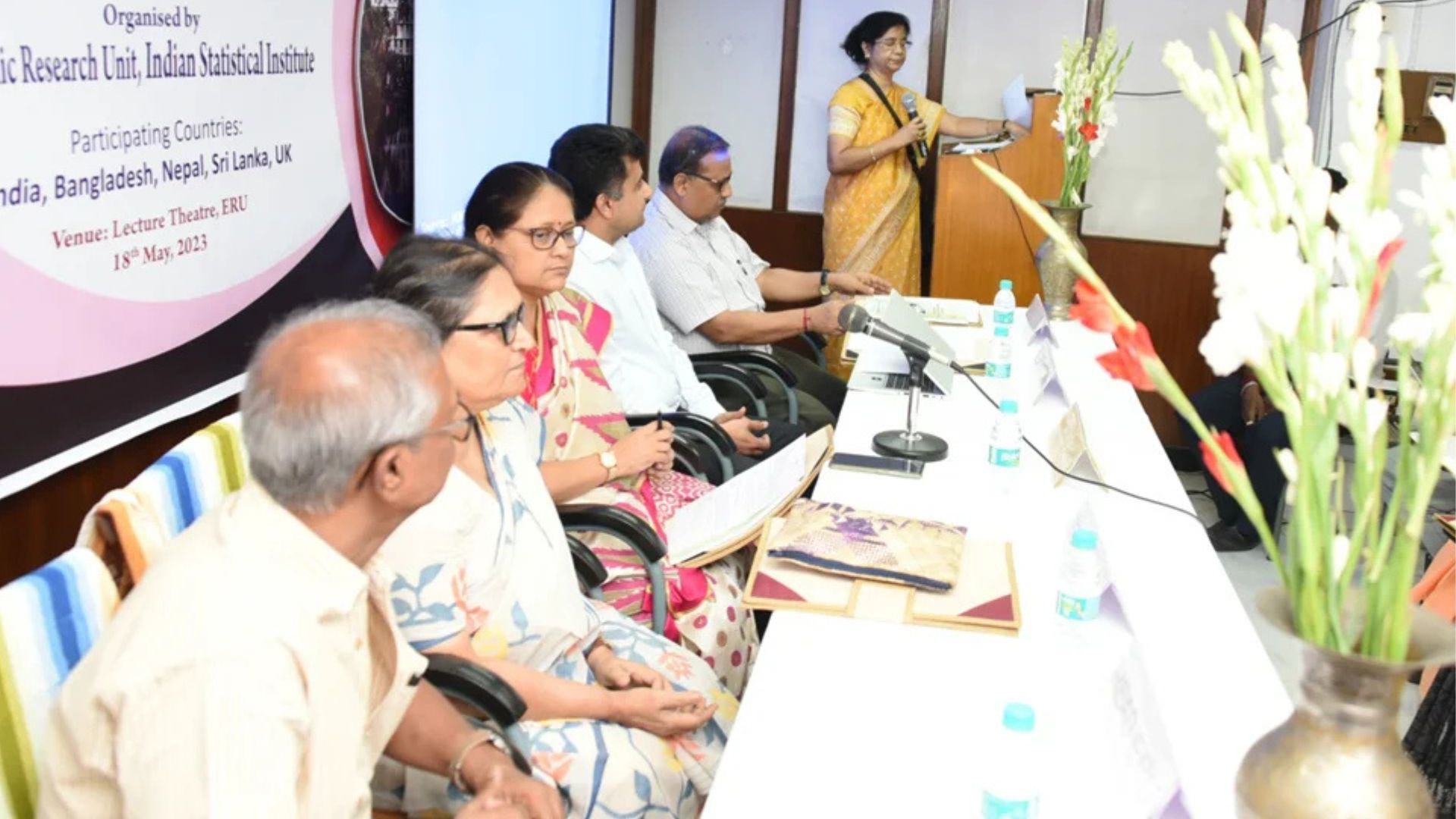 A diverse group of people seated at a table, including a woman in a wheelchair engaged in conversation.