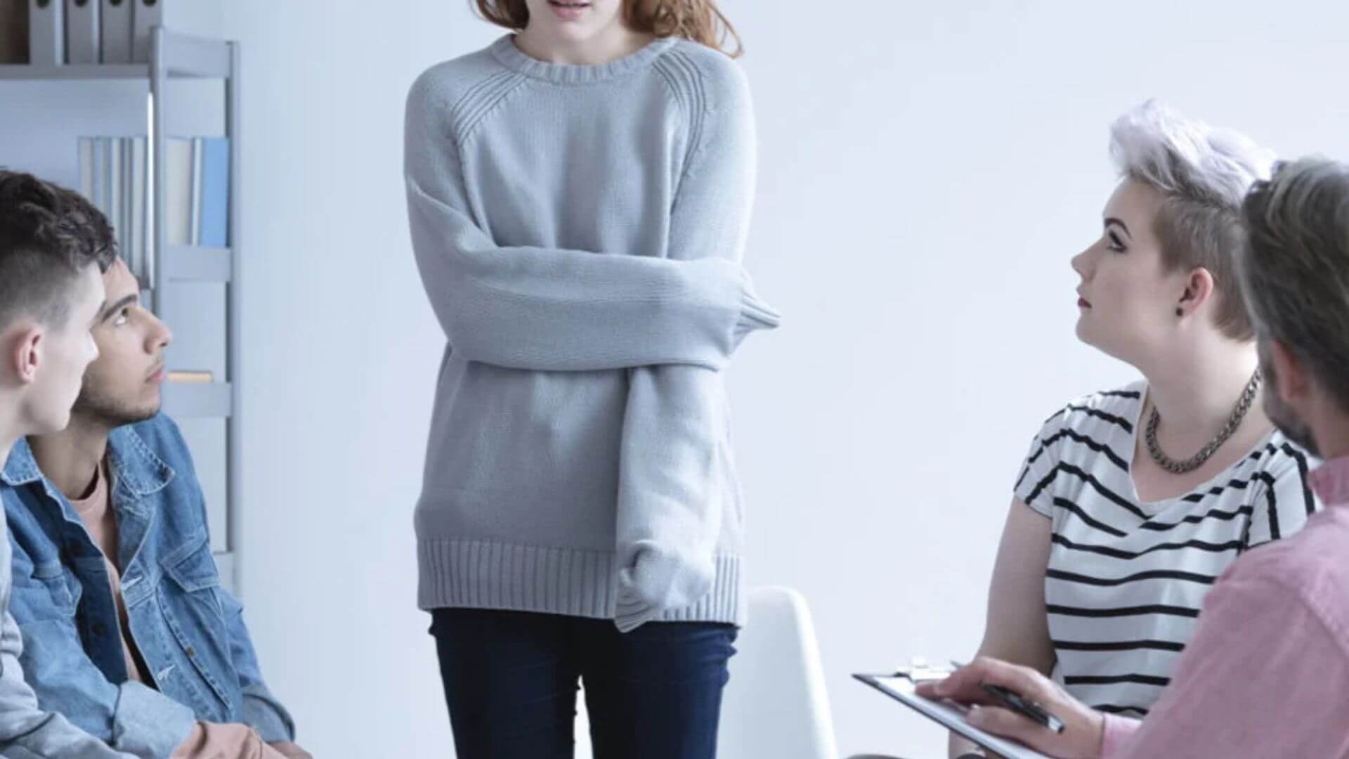 A young girl stands in front of a group of attentive people.